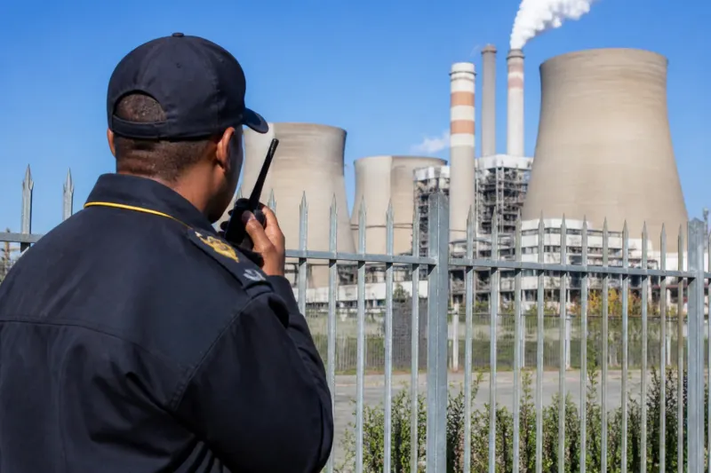 A warning sign in front of a power plant with a security fence.