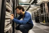 A technician checks network cables in a data center, highlighting infrastructure vulnerability.