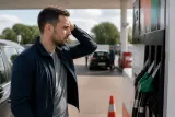 A concerned driver at a petrol station checking fuel prices